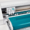 Close‑up plotter Silhouette Cameo 4 cortando vinil turquesa con alimentador de rollo | Tienda Revenato